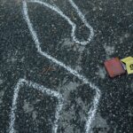 Crime scene with a chalk outline and evidence marker on asphalt.