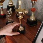 A close-up of a hand reaching for a shiny trophy on a wooden shelf, symbolizing success.