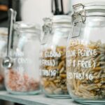 Set of glass jars with lid containing penne and elbow macaroni and various products on wooden shelf