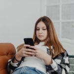 Teenage girl using smartphone while lounging on a sofa indoors.