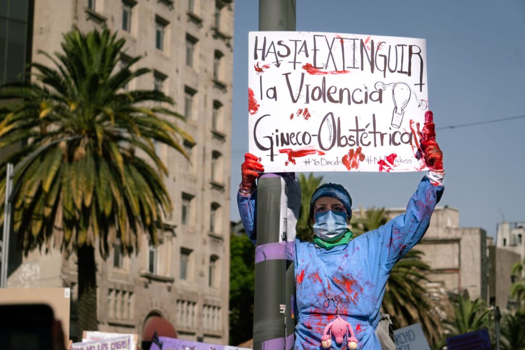 A woman participates in a protest against obstetric violence in Mexico City, holding a powerful sign.