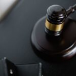 From above of wooden gavel on round surface near folders on table in courtroom