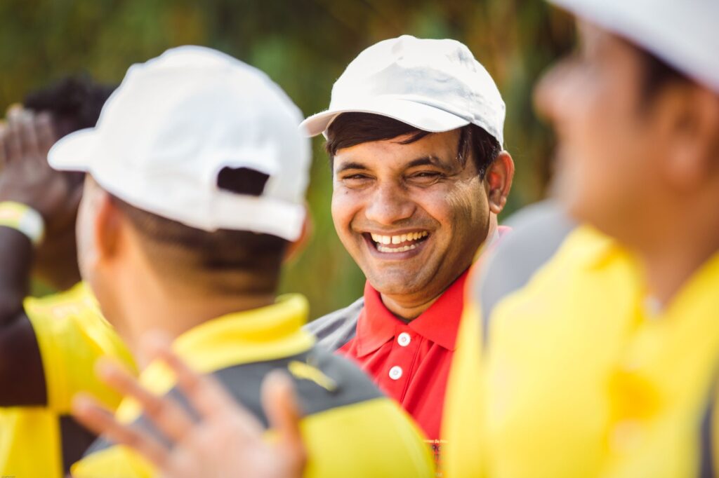 A joyful man in a white cap laughing during an outdoor event with friends. Casual attire and happy expressions.