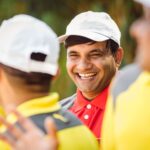 A joyful man in a white cap laughing during an outdoor event with friends. Casual attire and happy expressions.
