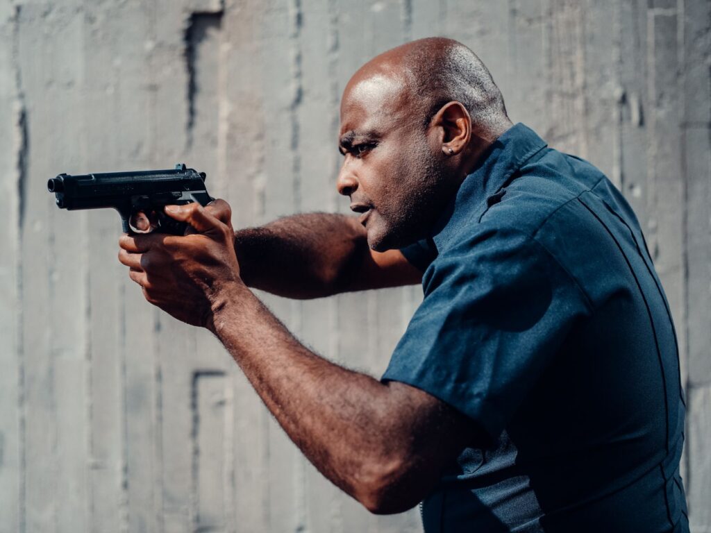 Police officer in uniform aiming a pistol outdoors, showing intensity and focus in a training scenario.