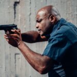 Police officer in uniform aiming a pistol outdoors, showing intensity and focus in a training scenario.