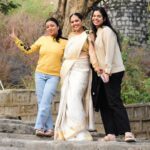 Three smiling women pose outdoors in colorful attire, embodying joy and friendship.