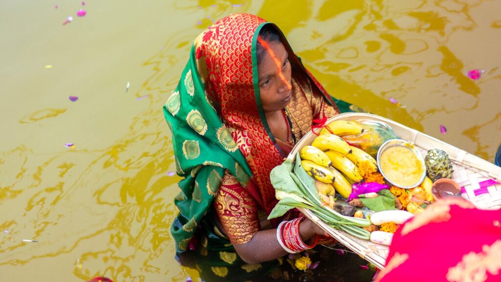 A woman participating in Chhath Puja, carrying traditional offerings in a river.
