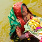 A woman participating in Chhath Puja, carrying traditional offerings in a river.