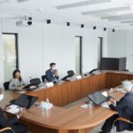 Business professionals wearing masks attending a conference meeting in a modern setting.