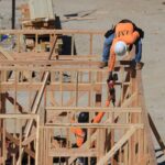 Two construction workers framing a wooden structure outdoors at a building site.