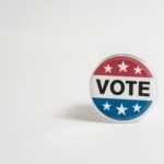 Close-up of a red, white, and blue vote button with stars on a white background.