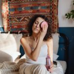 Woman with curly hair removes makeup using a cotton pad in a cozy, stylish bedroom.