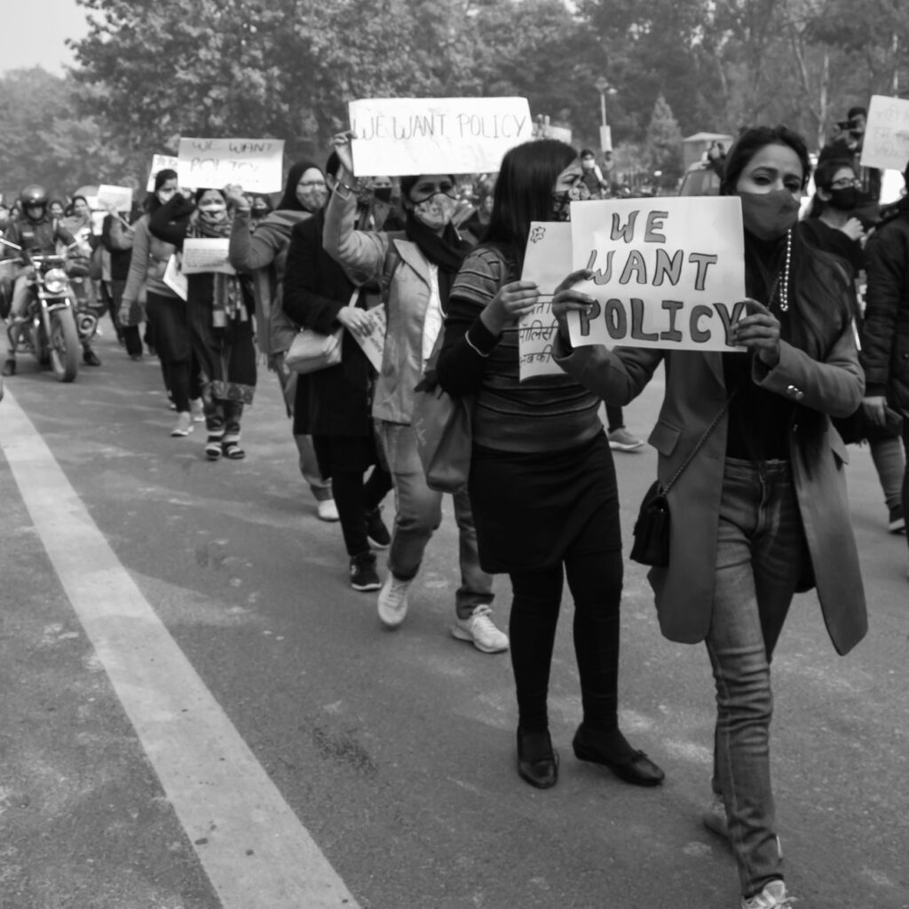 Black and white photo of a protest rally with people holding 'We Want Policy' signs.