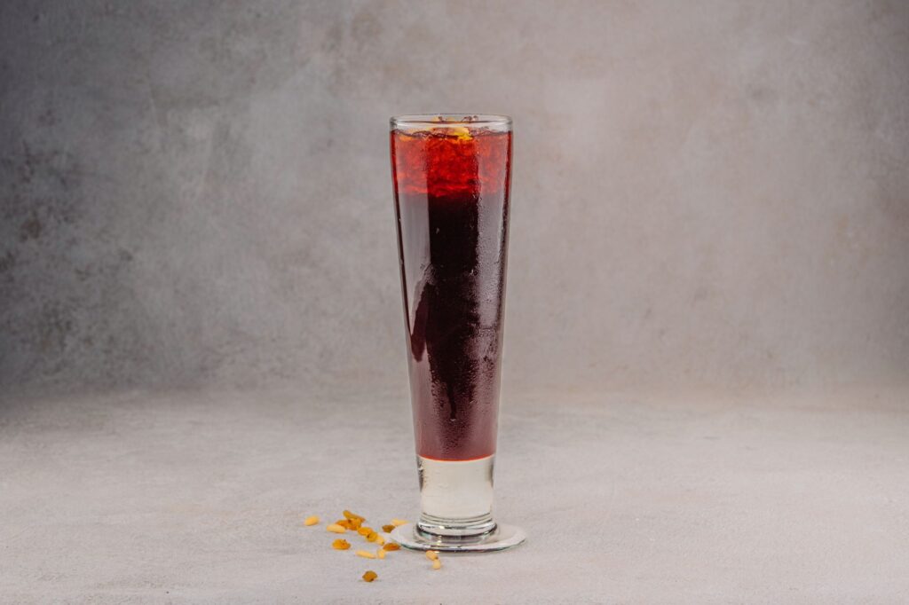 A refreshing red berry cocktail in a tall glass, perfect for a cool beverage on a gray background.