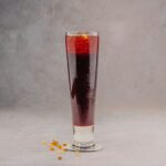A refreshing red berry cocktail in a tall glass, perfect for a cool beverage on a gray background.