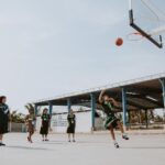 Group of children in school uniforms playing basketball outdoors on a sunny day.