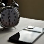 A classic silver alarm clock and modern smartphone placed side by side on a light surface.