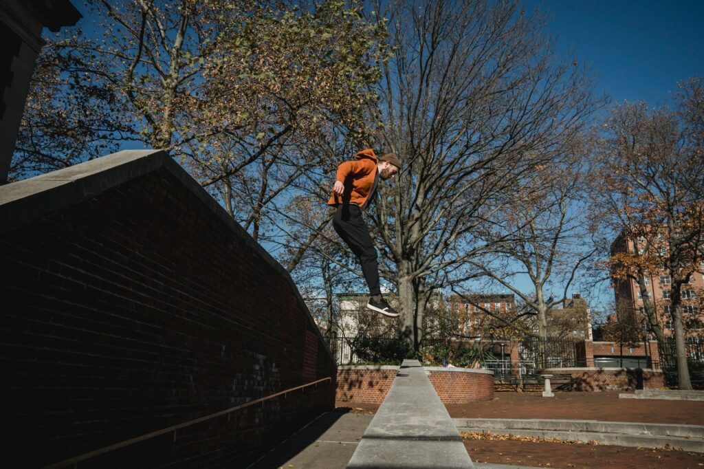 Side view full body sporty male tracer jumping from brick fence in autumn park in modern city