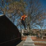 Side view full body sporty male tracer jumping from brick fence in autumn park in modern city