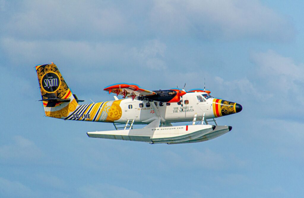 Vibrantly painted seaplane flying over the clear skies of Maldives, showcasing its colorful design.