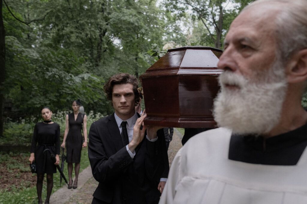 A group of people in a solemn funeral procession carrying a coffin outdoors.