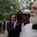 A group of people in a solemn funeral procession carrying a coffin outdoors.