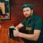 Man in festive St. Patrick's Day attire enjoying green beer at a pub.