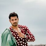 Fashionable portrait of a man on a Maldives beach in a polka dot shirt holding sunglasses.