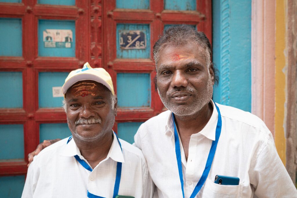 Portrait of two friendly local men in Varanasi, India, standing in front of a colorful door.