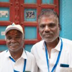 Portrait of two friendly local men in Varanasi, India, standing in front of a colorful door.