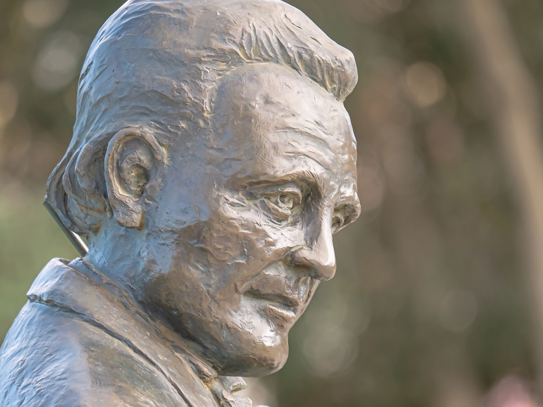 A detailed bronze sculpture capturing a serene expression of an individual outdoors.