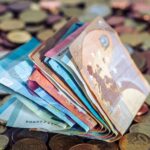 A stack of euro banknotes and scattered coins symbolize wealth and finance.