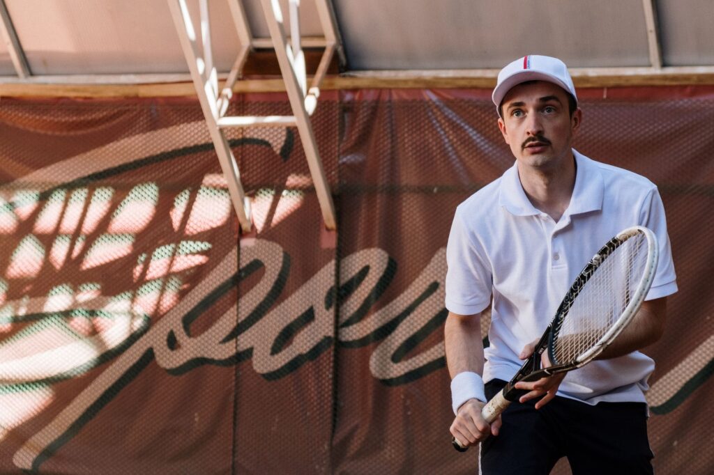 Young male tennis player in white attire prepares to play on a clay court.