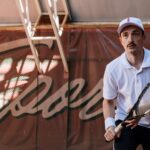 Young male tennis player in white attire prepares to play on a clay court.