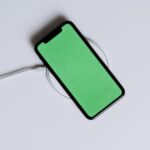 A minimalist smartphone with a green screen on a wireless charger, ideal for tech mockups.
