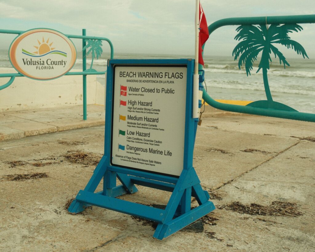 Beach warning flags sign in Volusia County, Florida, indicating hazard levels near public beach.