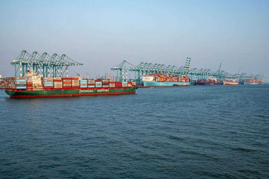 A bustling shipping port featuring container ships and crane operations under clear skies.