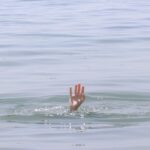 A hand reaching out of calm water on a sunny day, hinting at themes of rescue and serenity.