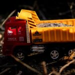 A vibrant toy dump truck filled with gravel, captured outdoors in natural lighting.