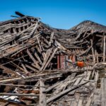 A dramatic view of a destroyed wooden building after a catastrophe, showing debris and structural failure.