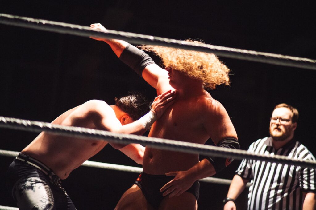 Dramatic wrestling scene with referee coaching competitors in the ring.