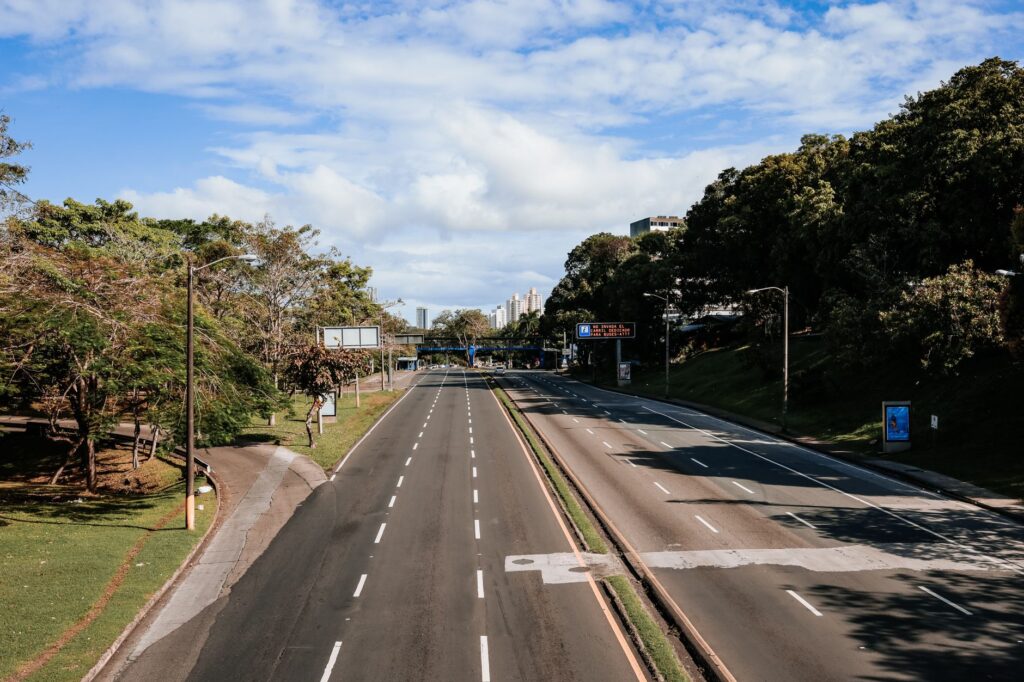 An empty highway lined with greenery, captured in clear daylight under blue skies.