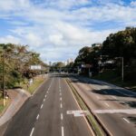 An empty highway lined with greenery, captured in clear daylight under blue skies.