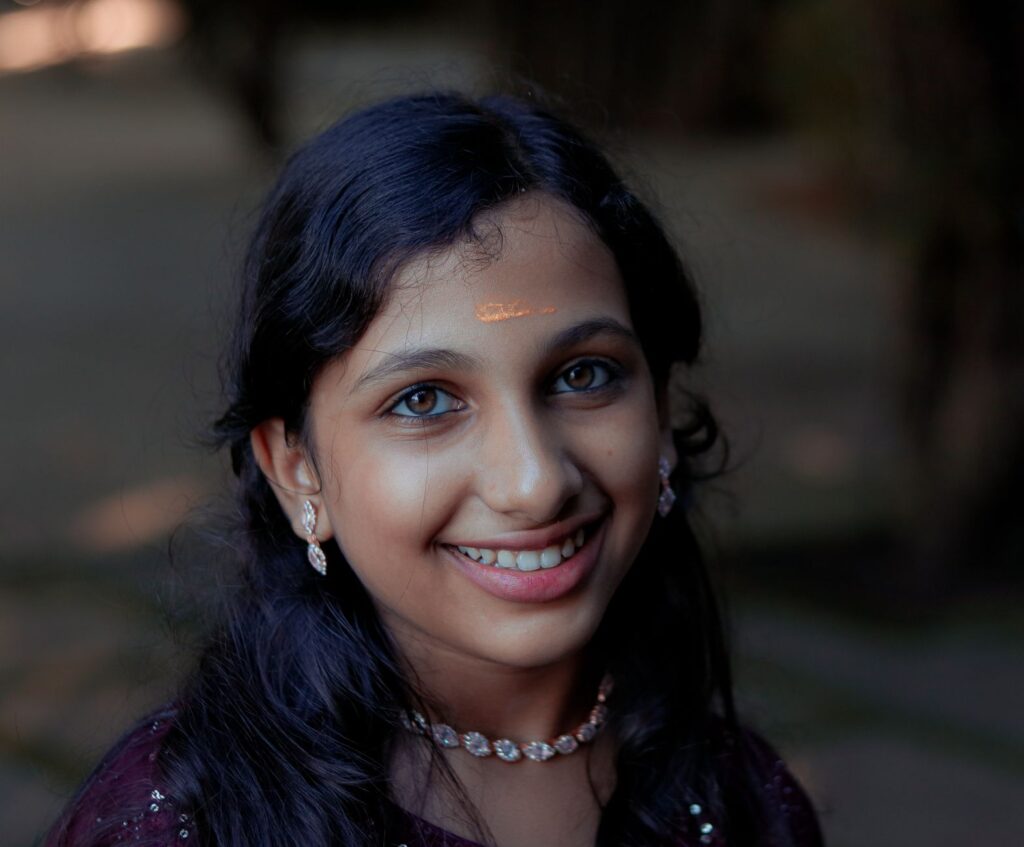 Portrait of a smiling girl with traditional jewelry and bindi in Thrissur, India, showcasing cultural beauty outdoors.