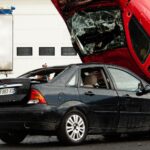 A thrilling car stunt crash with a red car flipped onto a black vehicle in an outdoor setting.