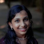 Portrait of a smiling girl with traditional jewelry and bindi in Thrissur, India, showcasing cultural beauty outdoors.