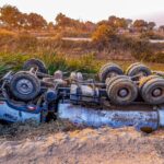 A truck overturned by the roadside on a rural dirt path during daytime.