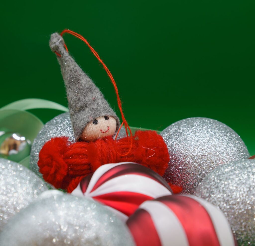 A cheerful elf Christmas ornament surrounded by glittery holiday decorations.