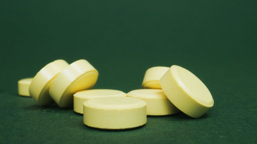 A close-up of scattered yellow tablets on a green surface, emphasizing their color and shape.